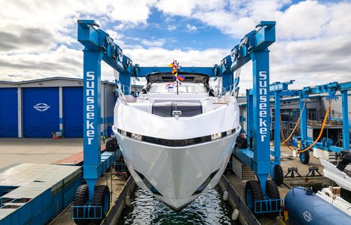 Frontal view of Sunseeker 100 Yacht being lowered in to water. Sunseeker facility visible in background.