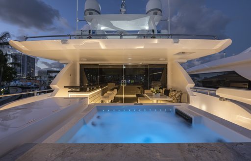 Overview of the aft bridge deck onboard ISSIMO, on deck Jacuzzi to starboard with interiors visible through glass doors.