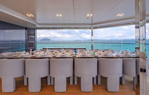 Formal dining set up onboard superyacht WANDERLUST. Total of 14 seats sat around table with extensive glazing in the background.