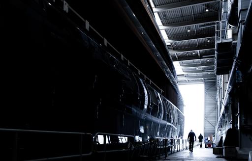 Ground level view of the Feadship Project 710 hull inside the construction shed prior to transit. With a couple of crew members walking alongside.