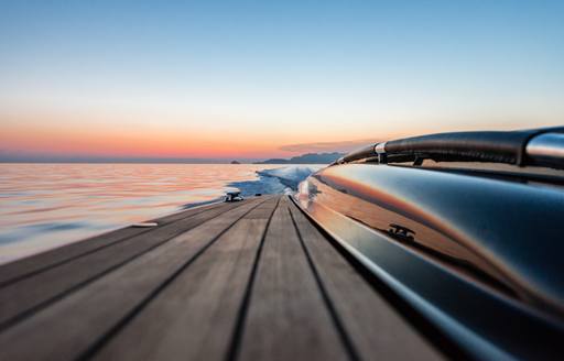 View down decking of Wooden Boats WB14 limousine tender, with sea and sunset in the background