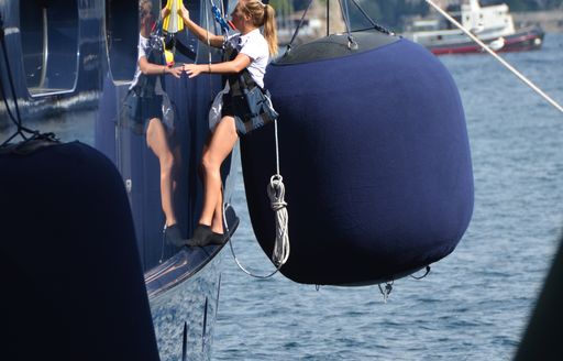 giant fender in background of female crew in harness washing yacht