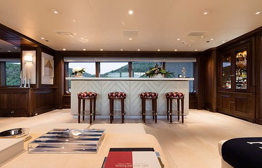 Wetbar onboard Feadship superyacht FLAG. Four stools lined up against wetbar, with wide glazing situated behind.