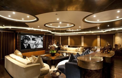 Interior lounge area onboard superyacht AV. Cream seating facing inwards around a coffee table, with a flatscreen TV on the wall.