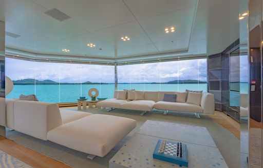 Upper lounge area in the upper salon onboard superyacht WANDERLUST. Cream seating surrounds a low coffee table with the whole area walled by unbroken wall of glazing. 