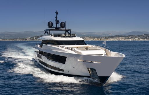 Frontal side view of Custom Line 140 bow, surrounded by sea with superyacht underway. Land in far distance in background. 