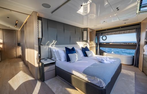 Master cabin onboard Sunseeker 100 Yacht, central berth facing starboard, with walkway in foreground and large window in background looking out over sea.