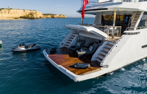 Overview of swim platform onboard the Sunseeker 100 Yacht. Jet Ski sat in water alongside yacht with sunloungers and water toys visible on platform.