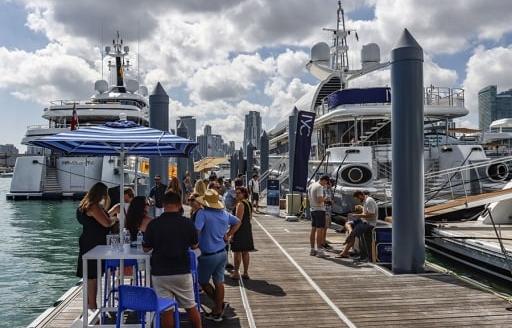 Ground-level view of Superyacht Miami with visitors walking along pontoon to berthed superyachts