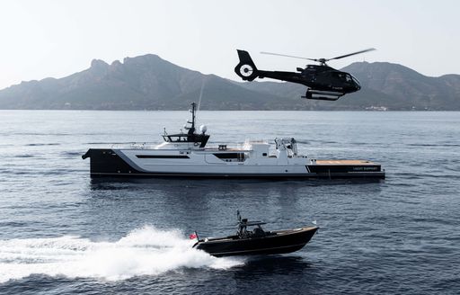 Superyacht Better Space surrounded by sea with tender alongside and an airborne helicopter