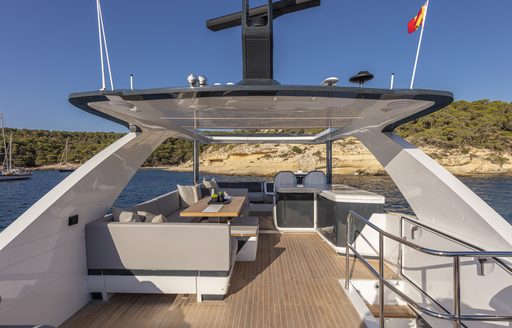 Overview of Pearl 62 flybridge, starboard facing sofa and shaded area under hardtop, surrounded by sea and sandy beach