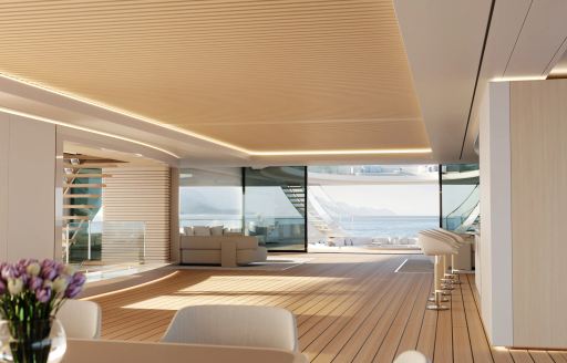 Overview of interiors onboard Feadship concept PURE. Wet bar to starboard with interior dining table in foreground. Open doors aft with exterior deck space visible.