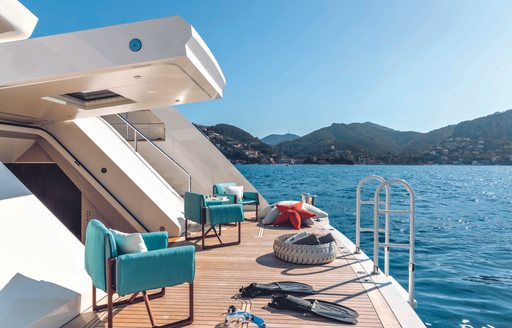 Beach club environment onboard CRN RIO superyacht. Side view with teal armchairs and water sports equipment visible.