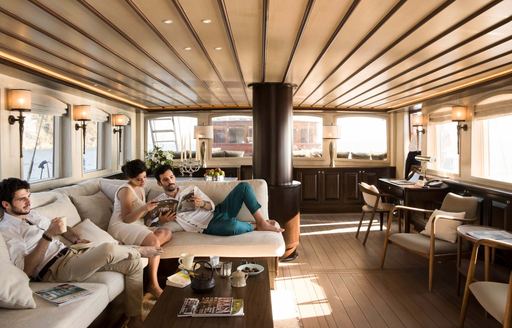 Three young adults relaxing in light colored salon of yacht.