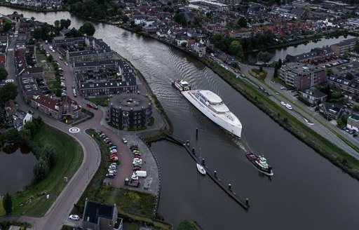 Aerial view of the Feadship superyacht Project 825 being escorted along a Dutch waterway.