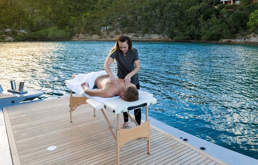 Masseuse massaging male guest on deck with water in background