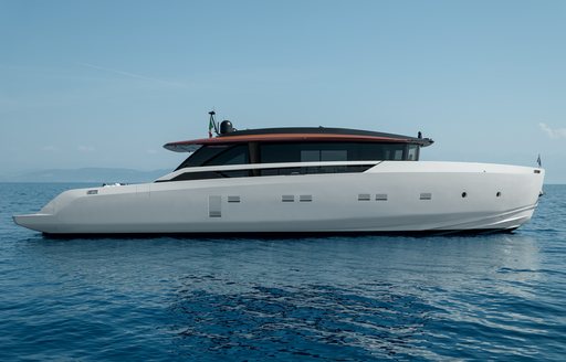 A starboard-side view of the Sanlorenzo SP92, with a black hardtop and a white hull, anchored in a blue sea