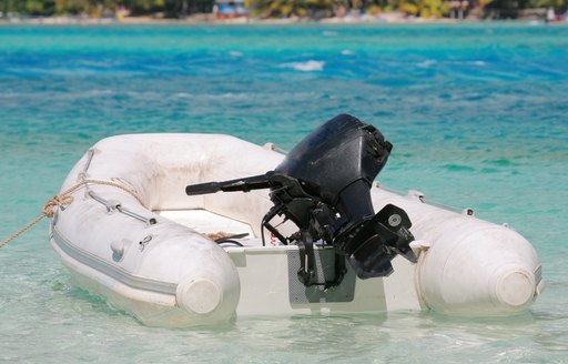 Stationary white RIB tender, with outboard motor, on clear water.