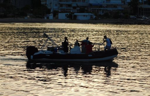 Workers on tender boat in early morning with coast and houses in the background