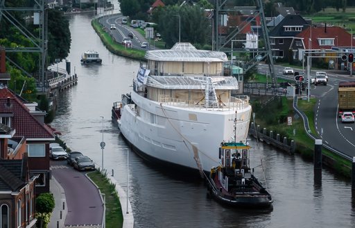 Feadship Project 825 underway on a Dutch waterway, with roads and houses either side.