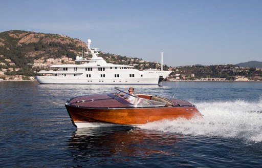 Classic tender boat moving at speed with superyacht and pictureque coast in the background