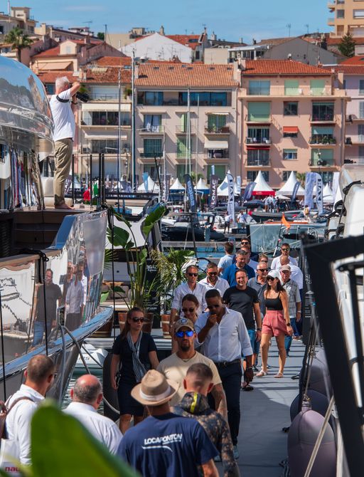 Overview of boardwalk at Cannes Yachting Festival with many visitors viewing superyachts on either side.