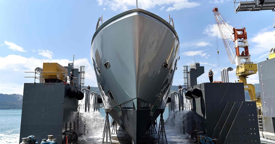 Frontal view of Sanlorenzo 44Alloy H1 hull in dock, surrounded by construction equipment, a crane and sea