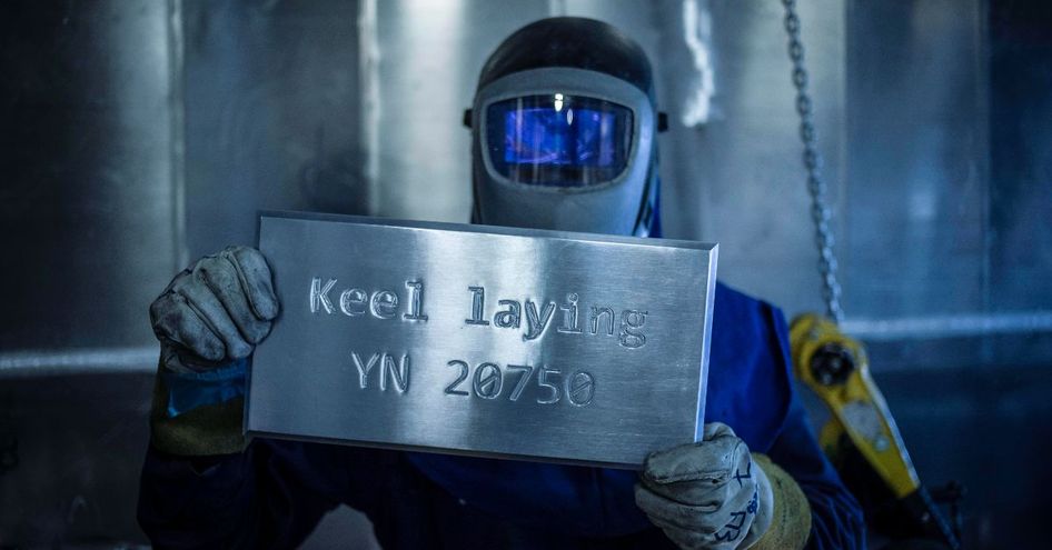 Shipbuilder holding up plaque reading 'Keel laying YN 20750'.