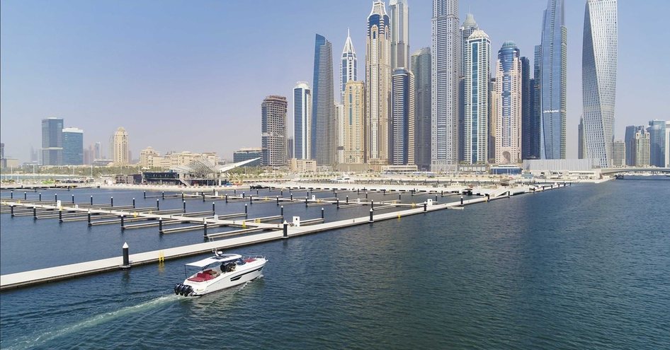 Small boat cruising past Dubai Harbour, surrounded by sea and Dubai skyline in background