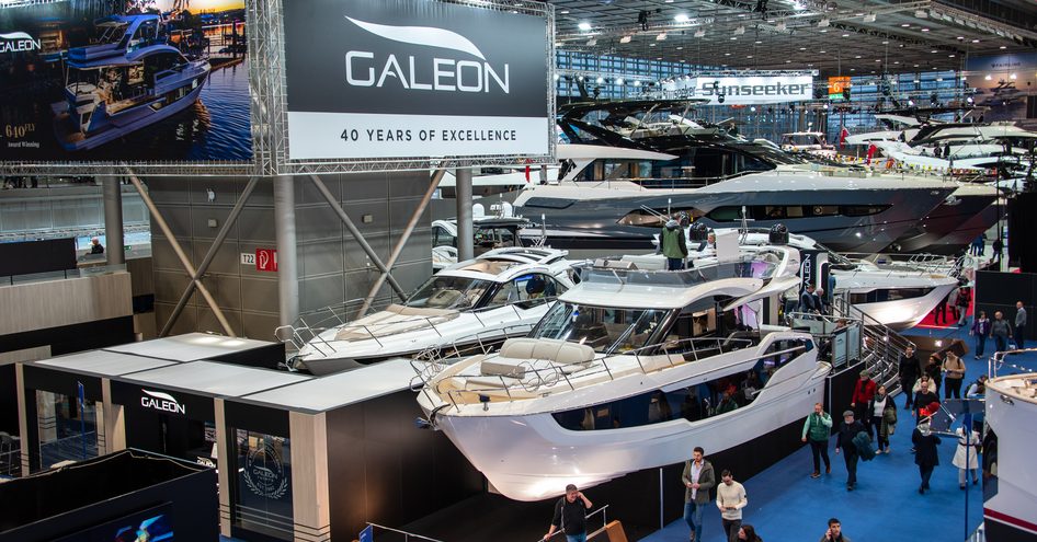 Overview of Galeon stand boot Dusseldorf, motoryachts on display with visitors walking around on blue carpet.