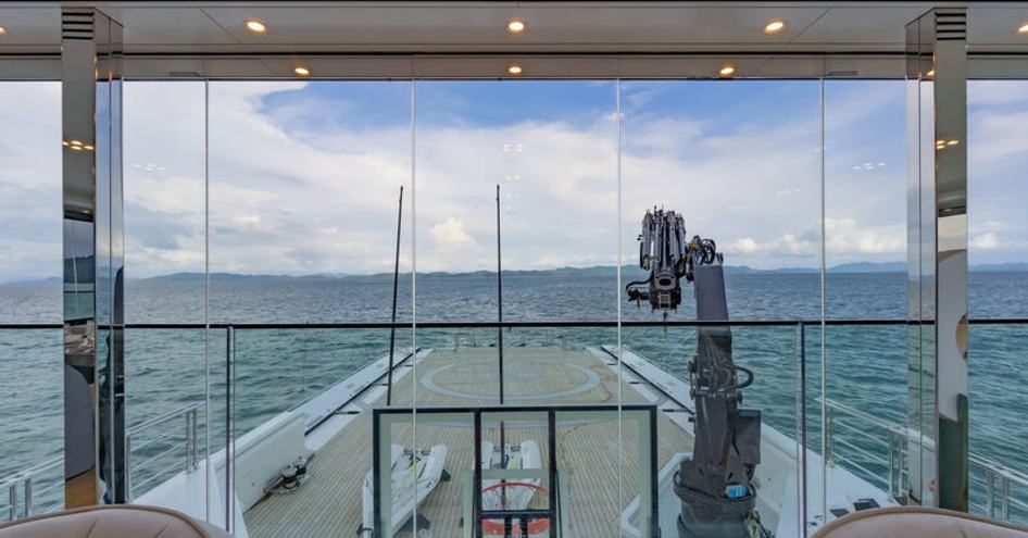 Overview of the  exterior deck onboard superyacht WANDERLUST. Vast glazing looks down over extensive deck laden with tenders and watersports equipment.