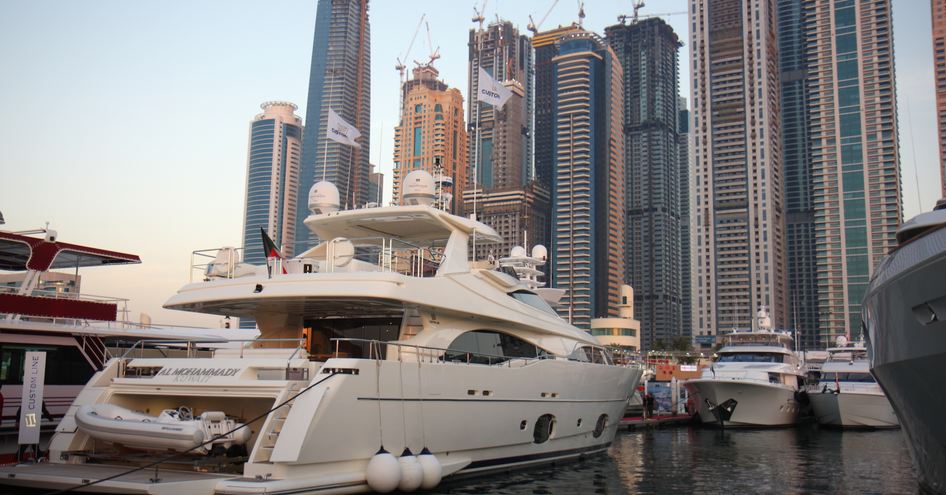 Superyachts moored at Dubai International Boat Show, aft view of a superyacht in foreground with others facing. Skyscrapers across background.