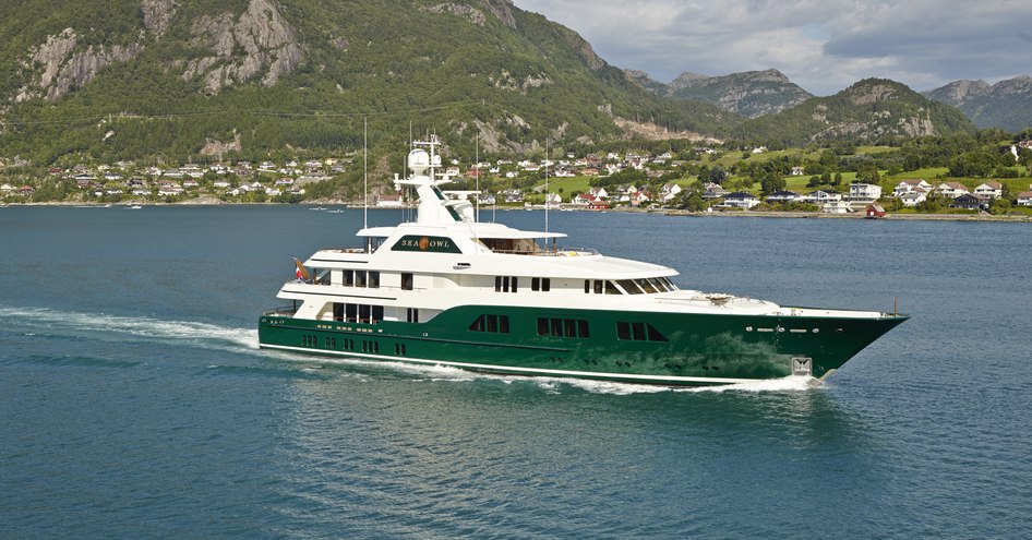 Superyacht Sea Owl underway, surrounded by sea and mountains in background.