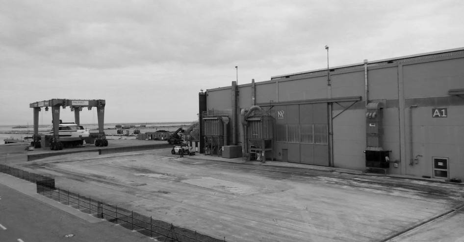 Black and white image of Palumbo Superyachts facility in Ancona. Sheds on the right with a dock on the left.