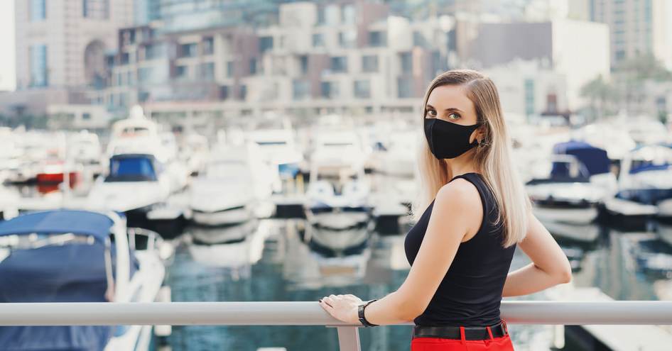 Female visitor in facemask poses in front of moored motor yachts