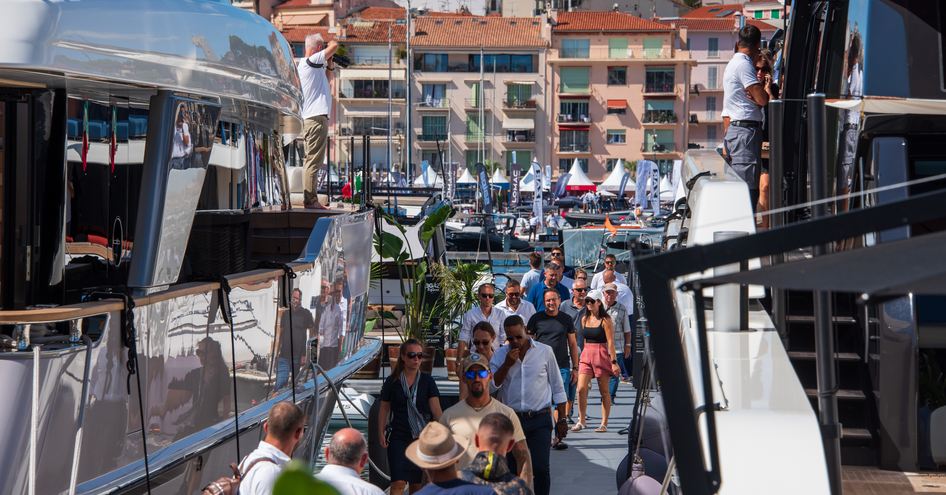 Visitors to Cannes Yachting Festival walking between yachts, with exhibitor tents visible in background.