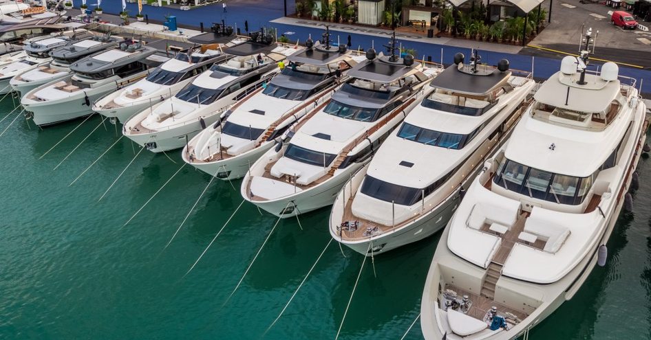 Motoryachts moored in line at Genoa International Boat Show, blue carpet in background.