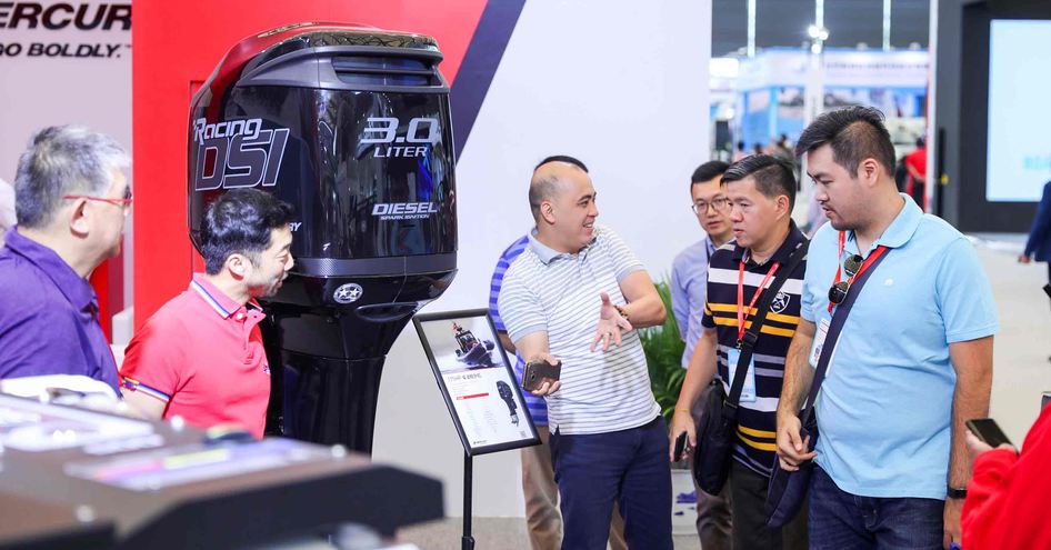 Exhibitor at China International Boat Show talking to visitors about outboard engine on display.