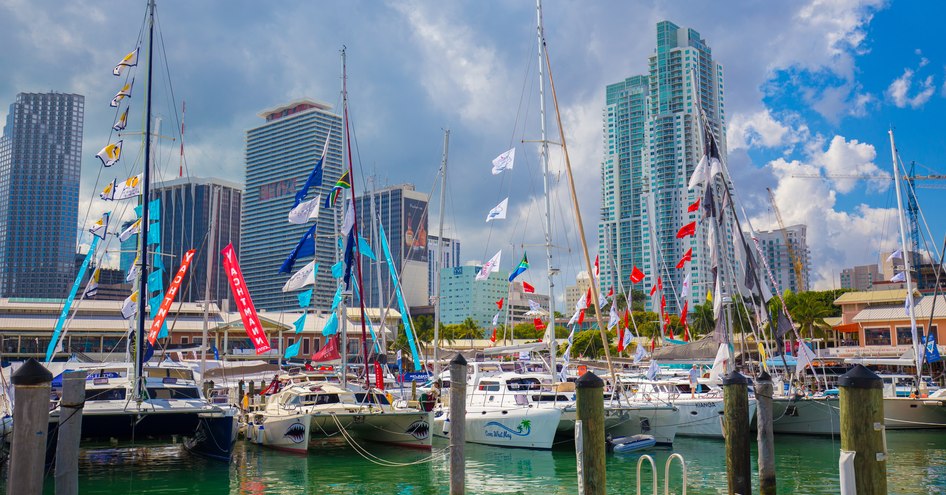 Line up of yachts berthed at the Miami International Boat Show, with Miami skyline in background.