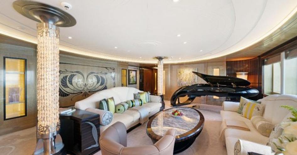 Lounge area onboard superyacht AMARYLLIS. White sofas and grey armchair face low coffee table with grand piano in background.