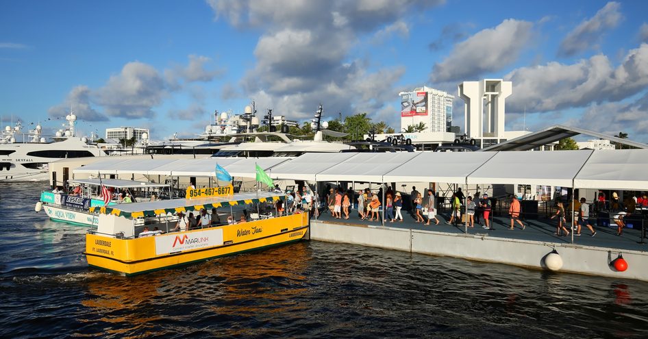 Water taxis at FLIBS, yellow taxi on the water awaiting passengers on pontoon, superyachts moored in background