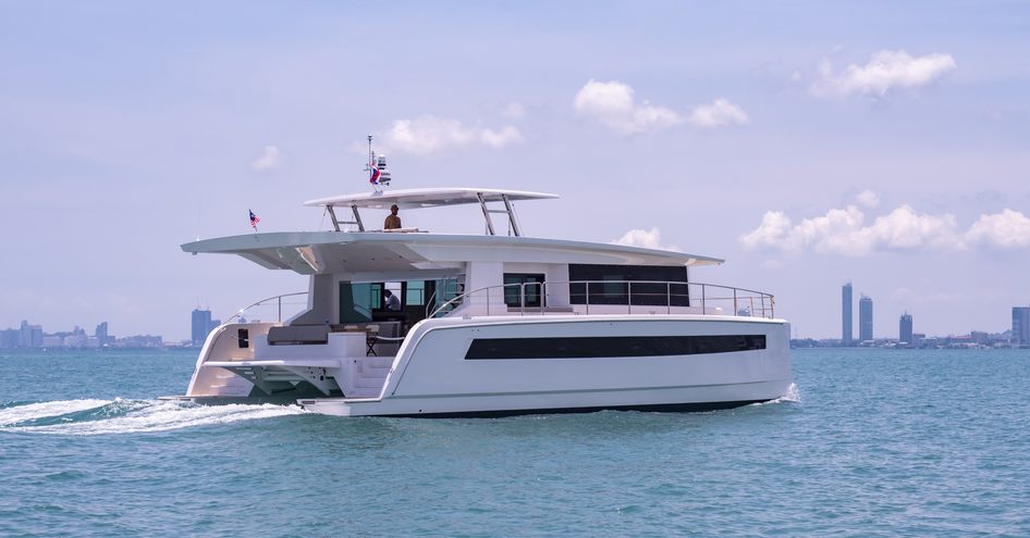 Aft angle view of Silent 60 catamaran underway, surrounded by sea with cosmopolitan skyscrapers on distant horizon.