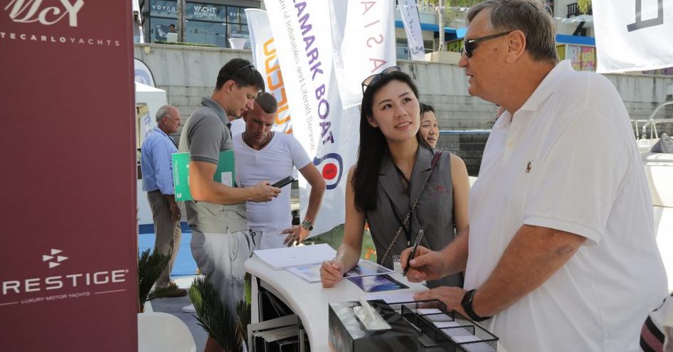 Male and female visitor to Thailand Yacht Show talking at a shipyard exhibit stand during show.