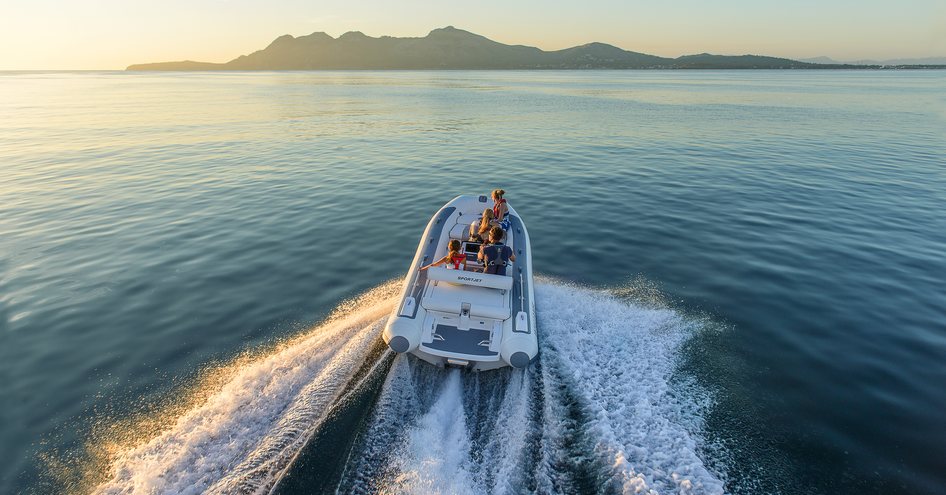 View from behind of a jet tender at sunset heading towards hilly coastline in distance