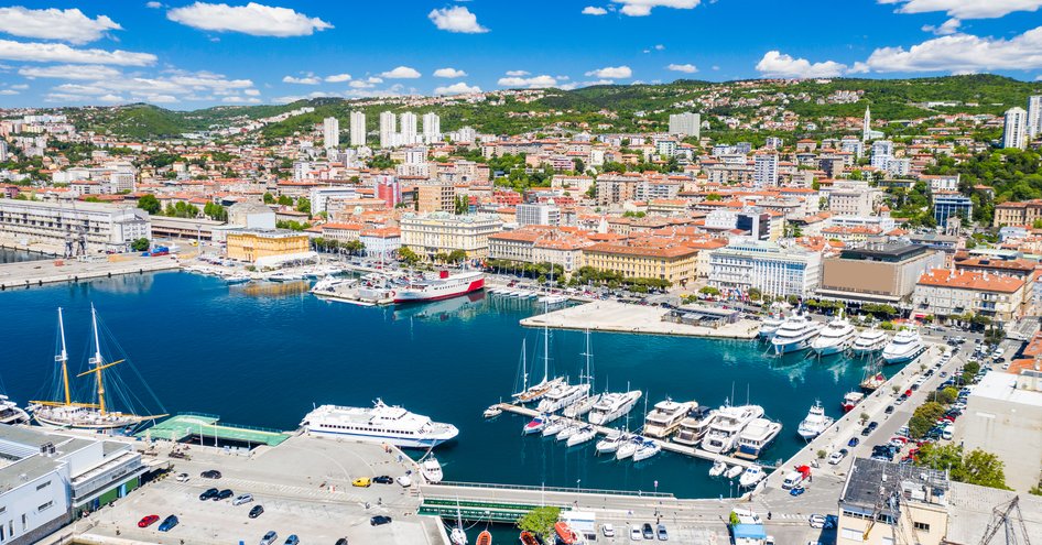 Elevated view over Rijeka harbour, with cityscape in background. Many motor yachts and sail boats moored. 