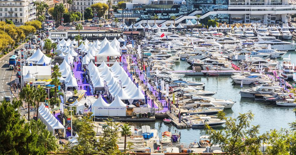 Exhibitor tents along the marina at the Cannes Yachting Festival. Many yachts berthed in marina.