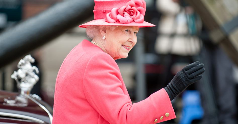 Queen Elizabeth II waving next to car, wearing pink suit and hat.