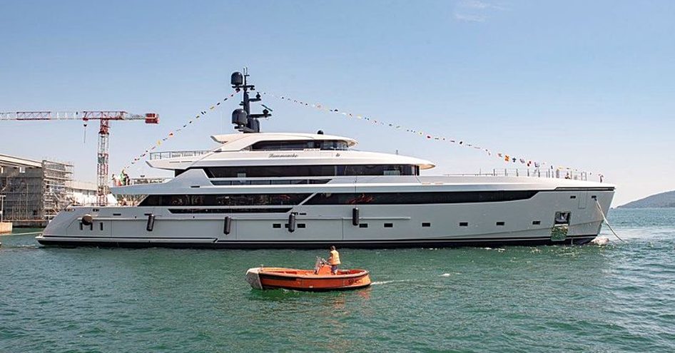 Side view of Sanlorenzo LAMMOUCHE heading out of dock during launch ceremony, adorned with flags and surrounded by sea