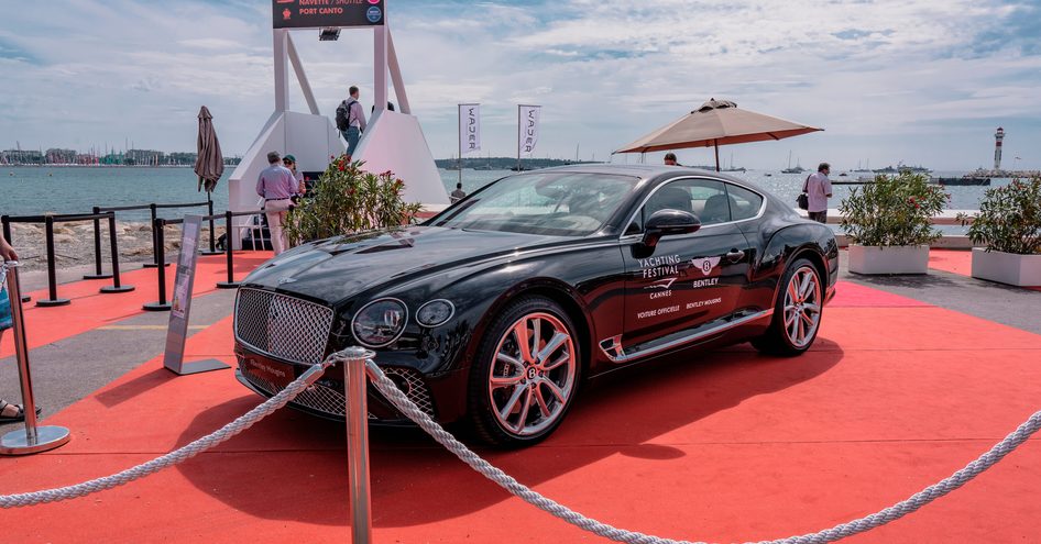 Premium car on display at Cannes Yachting Festival, sat on red carpet with sea in background.