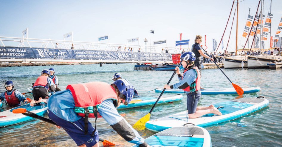 Group of young visitors at Southampton Boat Show trying out paddle boarding.